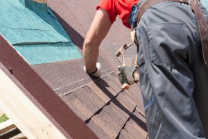 A roofing professional using a hammer while installing shingles 