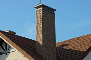 One big brown brick chimney on the roof of a house