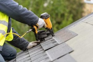 A worker with drill machine working on a top roof of a house.